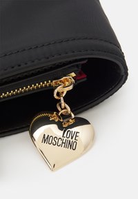 Černá látková taška uvnitř má zlatý zip a lesklý zlatý přívěsek ve tvaru srdce s nápisem "LOVE MOSCHINO."