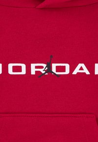 Red hoodie with a soft texture, featuring "JORDAN" printed in white and a black Jumpman logo on the front. Cozy design with a kangaroo pocket.