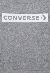 Felpa grigia realizzata in un tessuto morbido, con una patch rettangolare bianca che presenta il testo in grassetto "CONVERSE" e un grafico di una freccia.