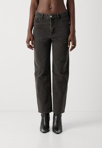 Jeans de mezclilla negra con un corte relajado, talle alto, diseño de cinco bolsillos y un desvanecimiento mínimo, combinados con botas negras hasta el tobillo con acentos metálicos.