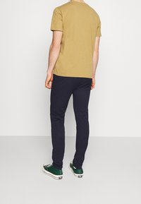 Kaki bomull t-shirt och marinblå byxor, bärs med gröna låga sneakers. Slät textur, avslappnad passform och enkel design.