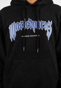 Sudadera con capucha negra y un bolsillo frontal. Presenta un texto bordado en azul que dice "Wasted Paris" y "Always Faithful". El texto tiene una tipografía estilizada.
