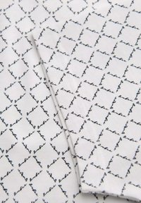 Bílá látka se opakujícím vzorem černého kurzivního písma ve tvaru diamantů. Hladká textura s jemným leskem.