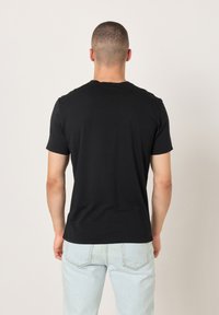 Crna pamučna majica s okruglim izrezom na vratu, kratkim rukavima i jednostavnim dizajnom na leđima. Kombinirana s svijetloplavim trapericama.