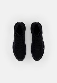 Paire de baskets de sport noires avec lacets, vues de dessus sur un fond gris clair uni.