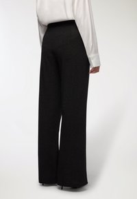 Czarne szerokie spodnie o gładkiej fakturze i wysokim stanem, zestawione z lekką, białą bluzką z długim rękawem.