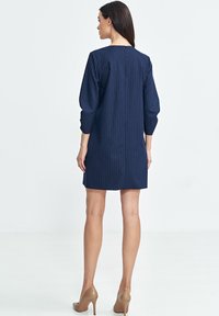 Granatowa sukienka w pionowe paski, z rękawami o długości trzech ćwiartek, z zapięciem na zamek z tyłu i prostym krojem, noszona z cielistymi szpilkami.