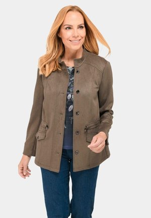 Braune Wildlederjacke mit Stehkragen, ausgestattet mit Knopfverschlüssen, zwei vorderen Taschen und einer strukturierten Oberfläche, getragen über einem blumigen Oberteil.