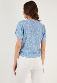Top floreale blu con maniche corte, scollatura rotonda e una texture morbida. Presenta motivi floreali bianchi su uno sfondo blu.