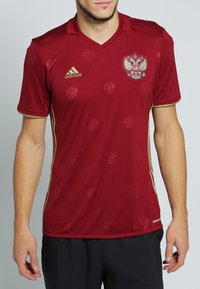 Röd polyester sporttröja med V-hals, gulddetaljer och prägling. Har ett märke på bröstet och en Adidas-logotyp.