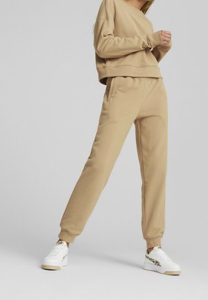 Osoba ubrana w beżowe spodnie dresowe i pasującą bluzę, do tego białe trampki z akcentami w panterkę.