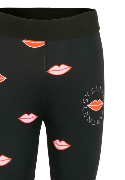 Leggings noirs avec un motif de lèvres colorées en rose et rouge, ornés d'un logo circulaire de marque accentué de strass sur le côté.