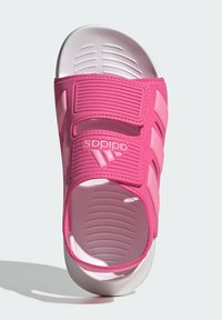 Roza Adidas natikača s dvema prilagodljivima trakama, teksturirano zgornje, kontrastno bela oblazinjena podplata, z logotipom.