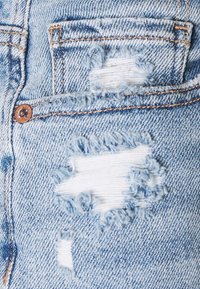 Svetle modrá džínovina se sepranými částmi. Pozoruhodné roztrhané okraje a viditelné detaily šití, s malou přední kapsou.