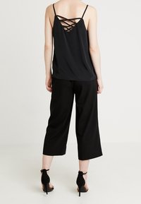 Camisola nera con sottili spalline, caratterizzata da un design incrociato sul retro, abbinata a culotte nere dal taglio ampio e sandali neri con tacco alto.