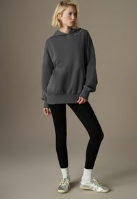 Tumma harmaa huppari, jossa on etutasku ja logodetalli, yhdistettyn�ä mustiin legginsseihin ja hopeisiin lenkkitossuihin. Silkkinen kangas, rento malli, pitkät hihat.
