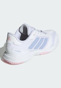 Zapatilla deportiva blanca con parte superior de malla, acentos en azul claro y diseño de tres rayas. Presenta detalles en la suela de color rosa y soporte reforzado en el talón.