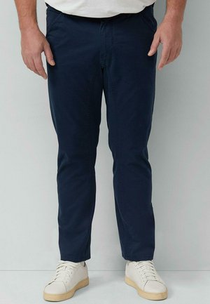 Dunkelblaue Chinos mit schmalem Schnitt, aus Baumwollstoff. Mit Reißverschluss und Fronttaschen, kombiniert mit weißen Sneakers.