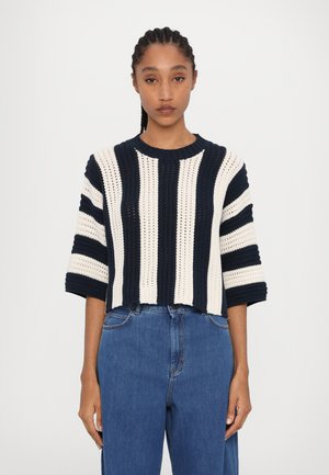 Pulover din tricot croșetat cu dungi orizontale bleumarin și crem, guler rotund, umeri căzuți și un design scurt. Asortat cu blugi albaștri.