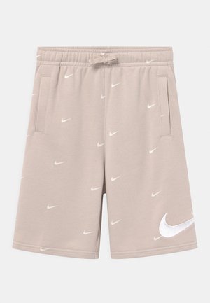 Beżowe spodenki Nike z elastycznym pasem, sznurkiem do regulacji, bocznymi kieszeniami oraz wieloma małymi białymi logo Nike swoosh i jednym dużym logo na nodze.