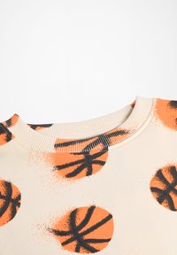 Top ar basketbola rakstu off-white audumā. Iezīmējas ar oranžām un melnām basketbola grafikām, ribinātu apkakli un gludu tekstūru.