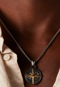 Metalen kompass-hanger met een gouden steraccent, aan een zilverkleurige ketting. De hanger heeft ingewikkelde patronen en details.