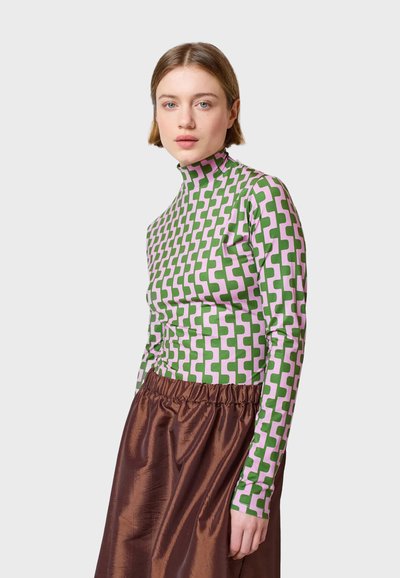Taillierte Langarmbluse mit grünem und rosa geometrischem Muster und hohem Kragen, kombiniert mit einem voluminösen braunen Satrock. Glatte Textur.