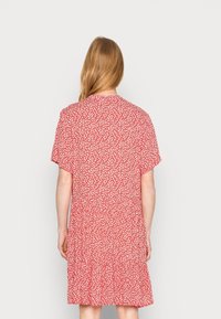 Robe florale rouge avec des manches courtes, taille froncée et ourlet en couches. Présente de petits motifs de fleurs blanches sur un fond rouge vif.