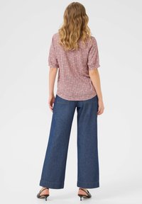 Czerwona i biała bluzka z krótkim rękawem o luźnym kroju, zestawiona z szerokimi, ciemnoniebieskimi dżinsami i czarnymi klapkami.