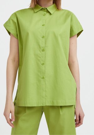 Zielona koszula na guziki z krótkimi, nakładanymi rękawami, wykonana z lekkiego materiału, z ostrym kołnierzykiem i bocznymi rozcięciami dla większej swobody ruchów.