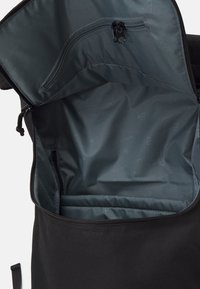 Sac noir avec une fermeture éclair sur le dessus. L'intérieur présente une doublure lisse et sombre, avec une poche zippée, ainsi qu'un compartiment pour l'organisation.