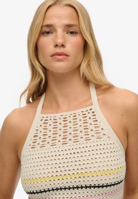 Gehaakte haltertop in crème met opengewerkte ontwerpen. Heeft veelkleurige strepen - geel, zwart, roze - over het lichaam.