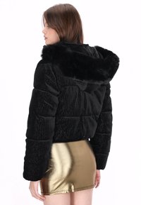 Czarna kurtka puchowa z kapturem wyłożonym sztucznym futrem, o połyskującej teksturze i pikowanym wzorze. Noszona z metaliczną złotą spódnicą mini.