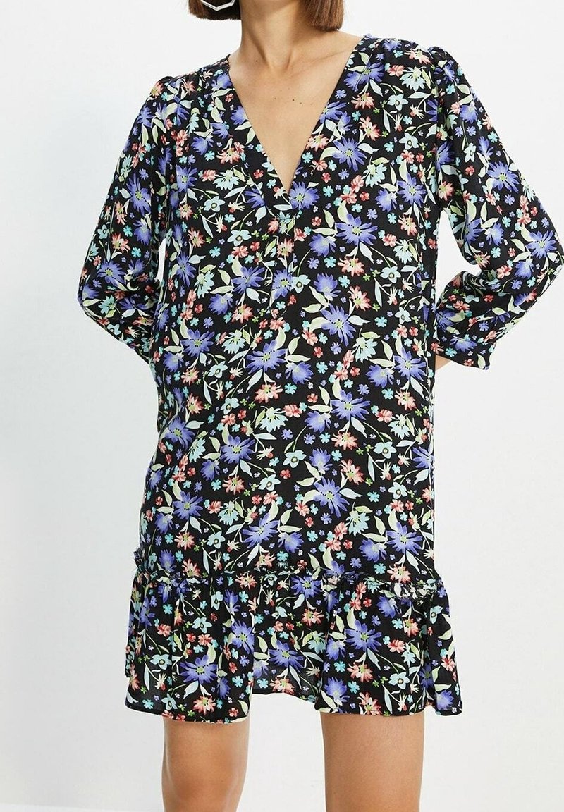 Robe noire à fleurs avec un décolleté en V, de longues manches bouffantes et un ourlet à volants. Le motif comprend des fleurs bleues, roses et vertes.