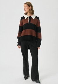 Bordeaux og sort stribet sweater med hvid krave og knaplukning, parret med sorte blondebukser med en bredere silhuet.