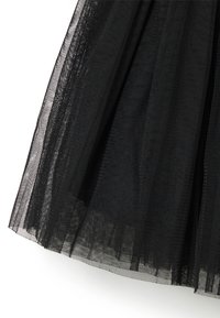 Schwarzer Tüllrock mit geschichteter Gestaltung und transparenter Textur, wobei Falten dem Stoff Volumen und Bewegung verleihen.