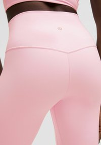 Różowe legginsy z wysokim stanem, wykonane z elastycznego materiału, z bezszwowym designem i małym logo z tyłu. Gładka tekstura.