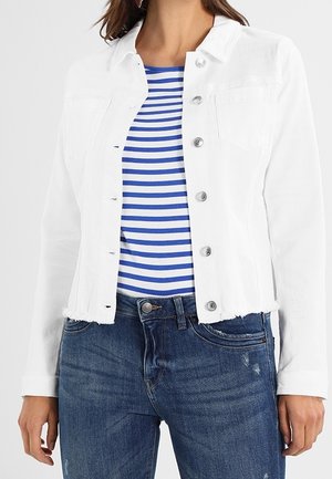 Femme portant une veste en jean blanche boutonnée sur une chemise rayée bleue et blanche et un jean bleu.