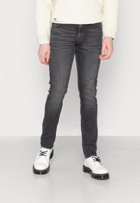 Jeans noirs slim en denim, avec un délavage moyen et un léger effet d'usure. Portés avec des chaussures blanches et un haut de couleur claire.