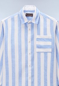 Camisa de lino a rayas en azul claro y blanco con cierre de botones, un bolsillo en el pecho con rayas horizontales y un cuello clásico.