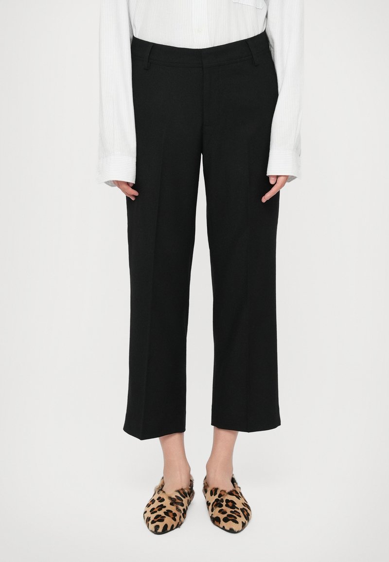 Pantalons noirs ajustés avec une coupe droite et une longueur cropped. Portés avec des chaussures à enfiler imprimé léopard. Une chemise blanche à boutons est visible.