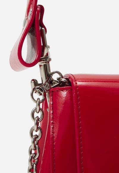 Red patent leather handbag corner with a silver chain and clasp. Features smooth texture, structured shape, and curved handle attachment.