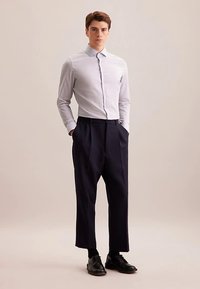 Lichtgrijs overhemd met knopen en een gestructureerde kraag, gecombineerd met marineblauwe, hoogtaillierte broek. Zwarte schoenen maken de outfit compleet.