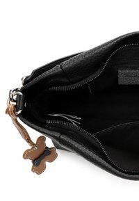 Sort læderhåndtaske med en tekstureret overflade, der har en lynlåslukning og en brun læder sommerfuglevedhæng fastgjort til siden.