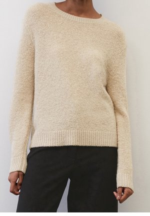 Pull en tricot couleur crème avec un col rond, des poignets et un ourlet côtelés. Texture douce et coupe décontractée, associé à un pantalon noir.