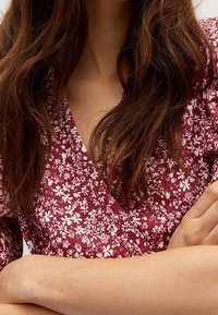 Bordo sukienka w kwiaty z białymi detalami, z dekoltem w kształcie litery V i krótkimi rękawami, wykonana z lekkiego materiału. Widoczne hafty.