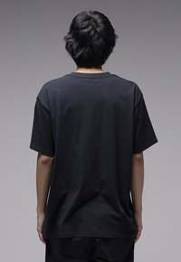 Μαύρο βαμβακερό μπλουζάκι με χαλαρή εφαρμογή, στρογγυλή λαιμόκοψη και κοντά μανίκια, φαίνεται από πίσω σε γκρι φόντο.