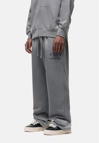 Gray sweatpants with a relaxed fit, drawstring waist, and printed black text. Made from soft fabric, featuring side pockets and ribbed cuffs.