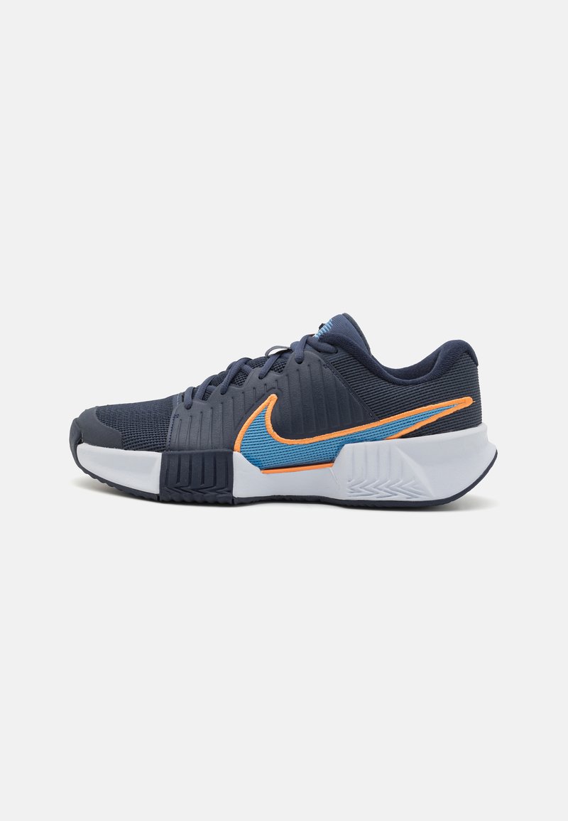 Nike sportssko med en navy mesh overdækning med teksturerede linjer, orange og blå accenter, en hvid mellemsål og en fleksibel gummiydersål.
