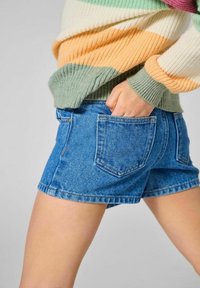 Denim kratke hlače v svetlo modri barvi, z dvema zadnjima žepoma in raztrganim robom. V kombinaciji z zeleno, breskovo in belo črtasto pleteno puloverjem.